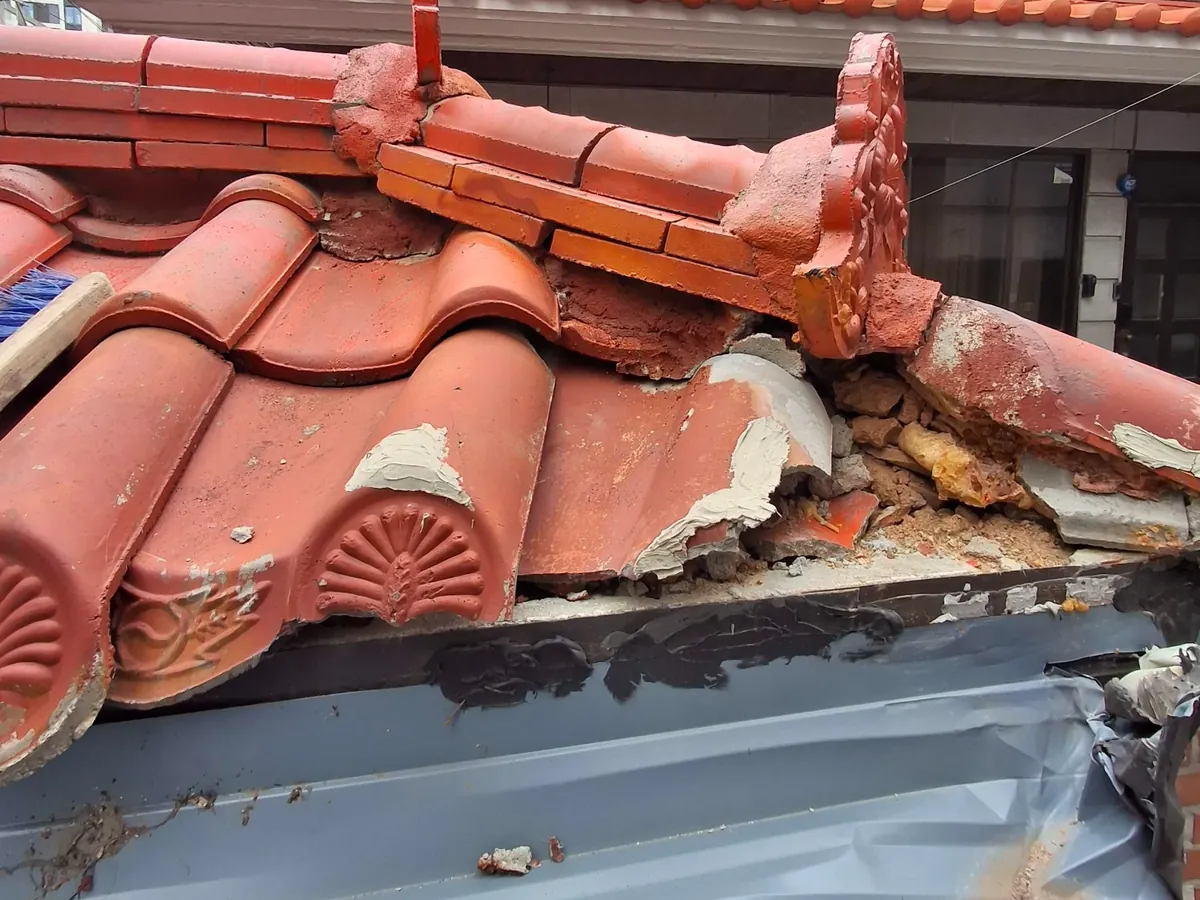 벽돌 대문 지붕 처마 모서리에서 기와가 깨지고 몰탈 고정층이 떨어진 교체 전 상태